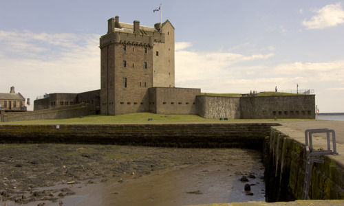 The imposing Broughty Castle from a distance, with a beach at low tide in the foreground