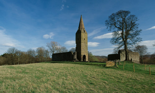 The tall church spire and ruins of Restenneth Priory on a field surrounded by trees