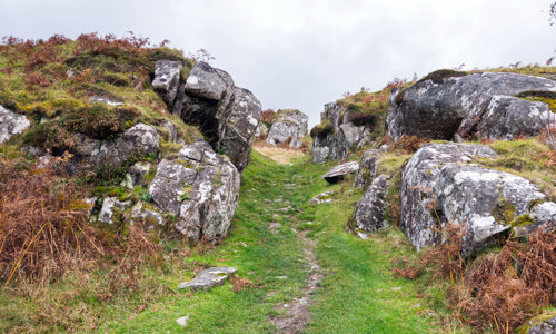 A path leading into the stone fort, which consists of ruined stone walls amongst rocks and grassy surfaces.