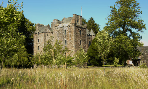 Well-preserved Elcho Castle with its several towers, surrounded by trees and fields.