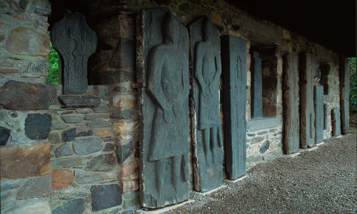 Several large sculptured stones portraying people in various poses are propped up against a roofed wall.