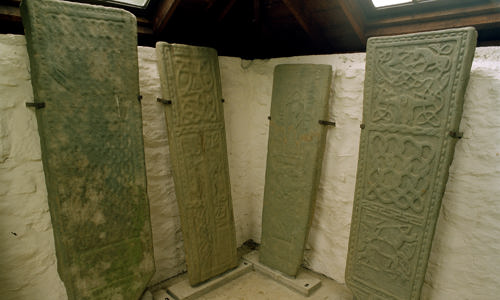Four tall sculptured stones propped against a white wall inside a building.