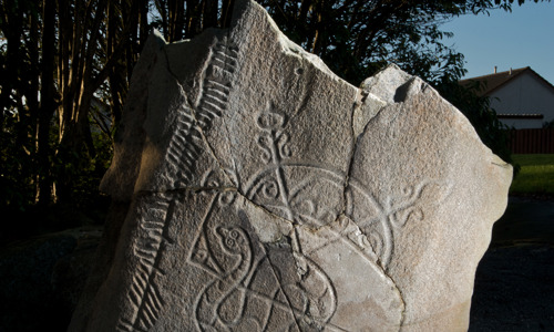 The large Brandsbutt stone at night, illuminated from one side which makes the intricate carvings stand out.