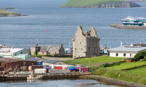 Scalloway Castle seen from a distance, surrounded by more modern houses and boats