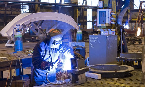 A welder wearing safety equipment welds a piece of metal in an industrial environment 