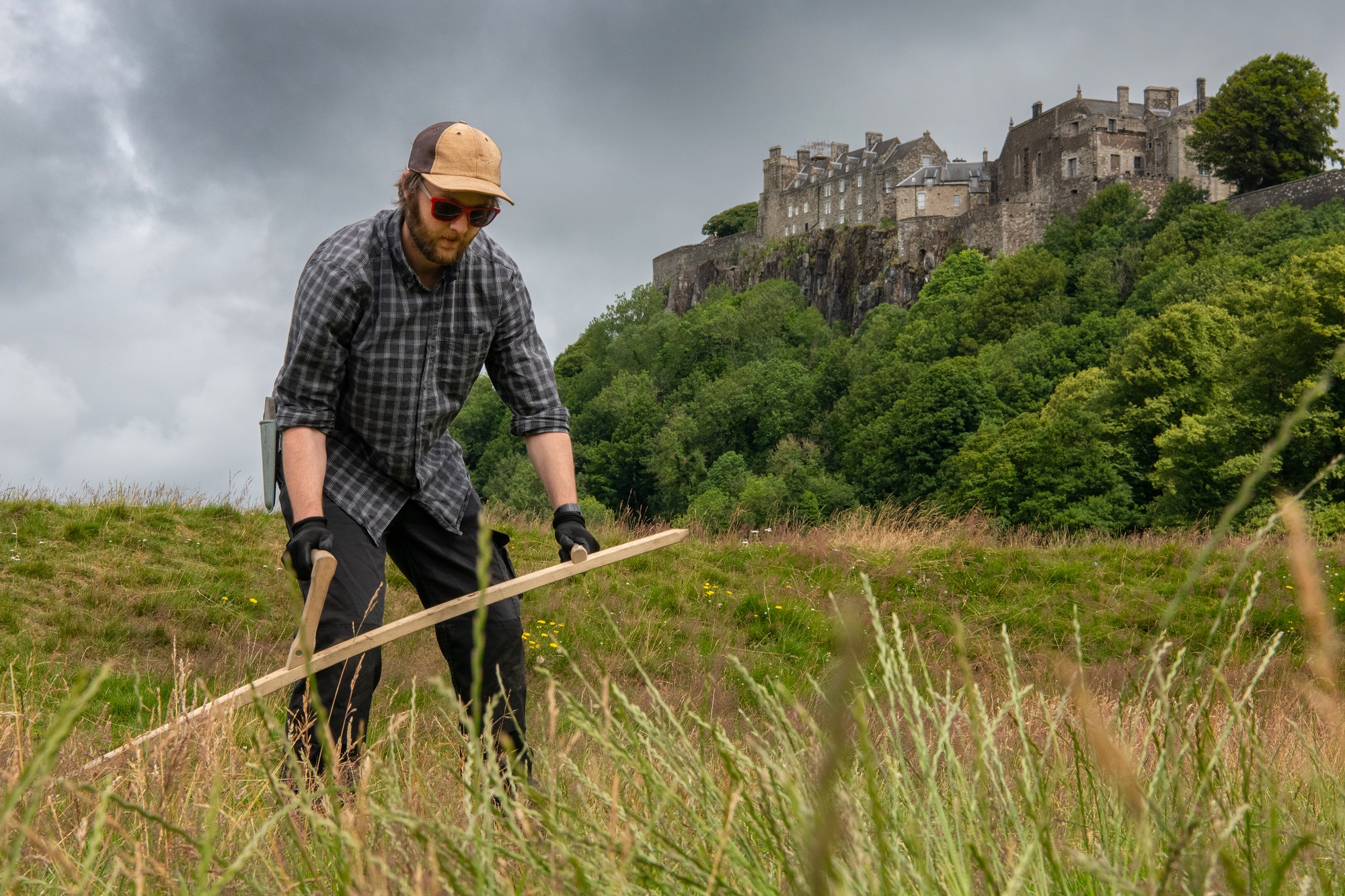 A man cutting grass with a scythe with a castle in the background