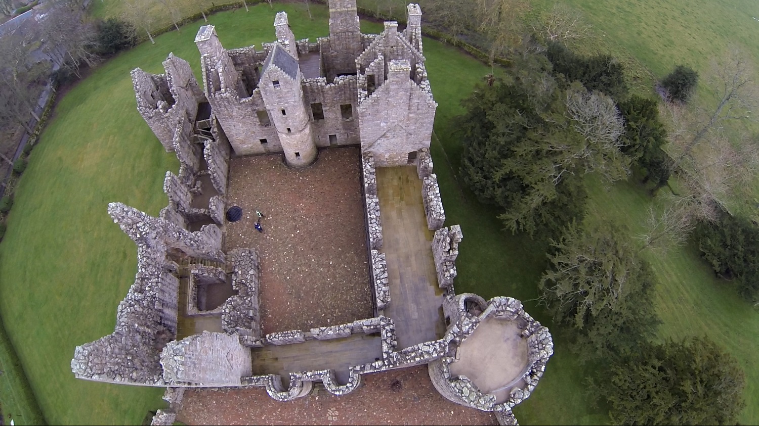 Aerial view of Tolquhon Castle’s roofless stone ruins, showing interior walls, towers, and surrounding lawns and trees.