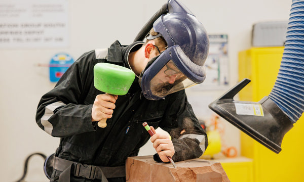 An apprentice in PPE working on a piece of stone