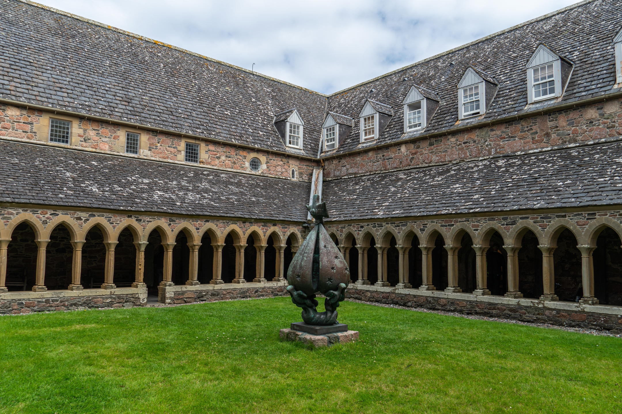A historic abbey courtyard, featuring a grassy square with a large sculpture 