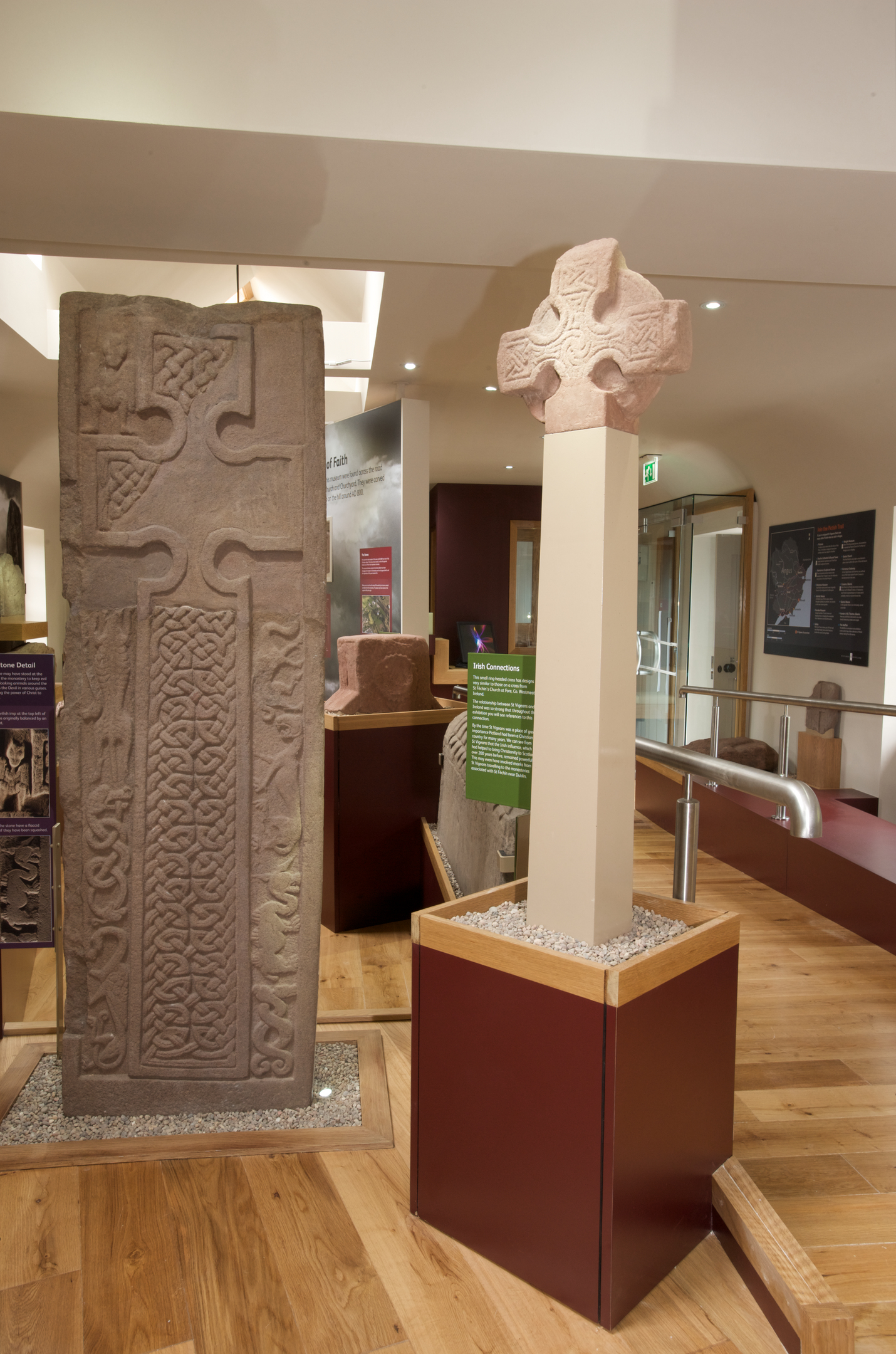 A tall Pictish cross‑slab stands next to a reconstructed sandstone cross mounted on a pillar. 