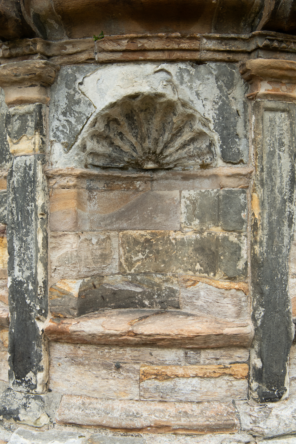 A weathered stone wall, with a circular and shell design in the centre. 