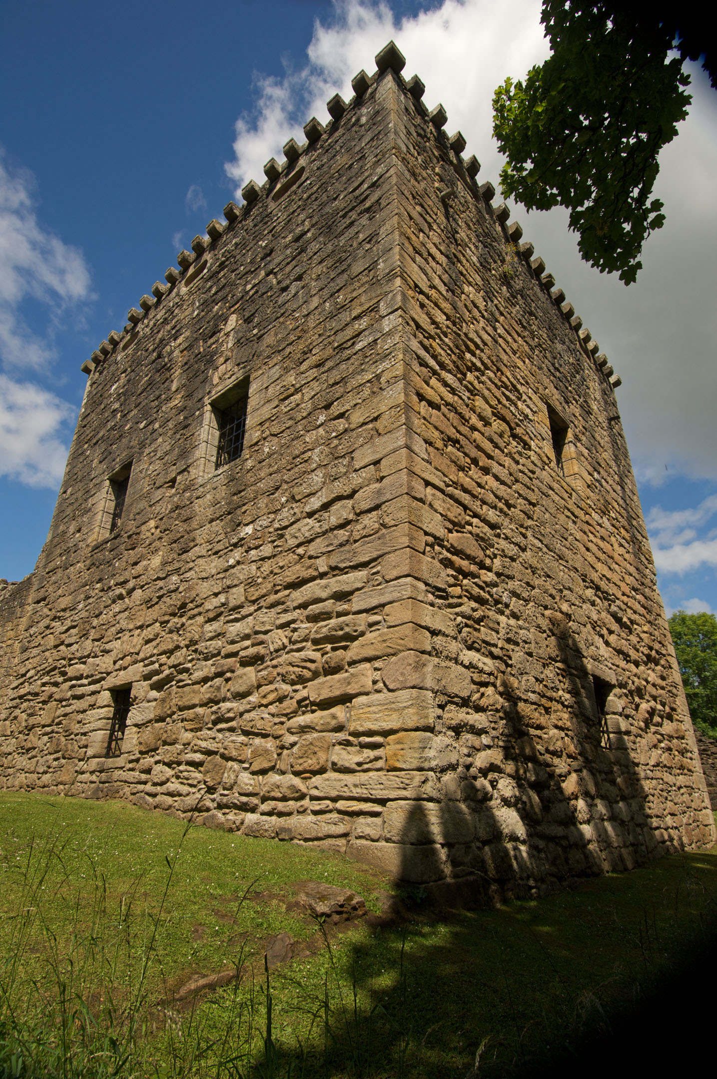 Tall square tower with stone walls and grassy foreground under blue sky.