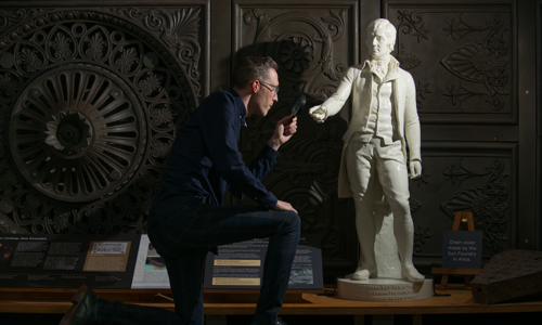 A statue of Robert Burns is inspected with a magnifying glass 