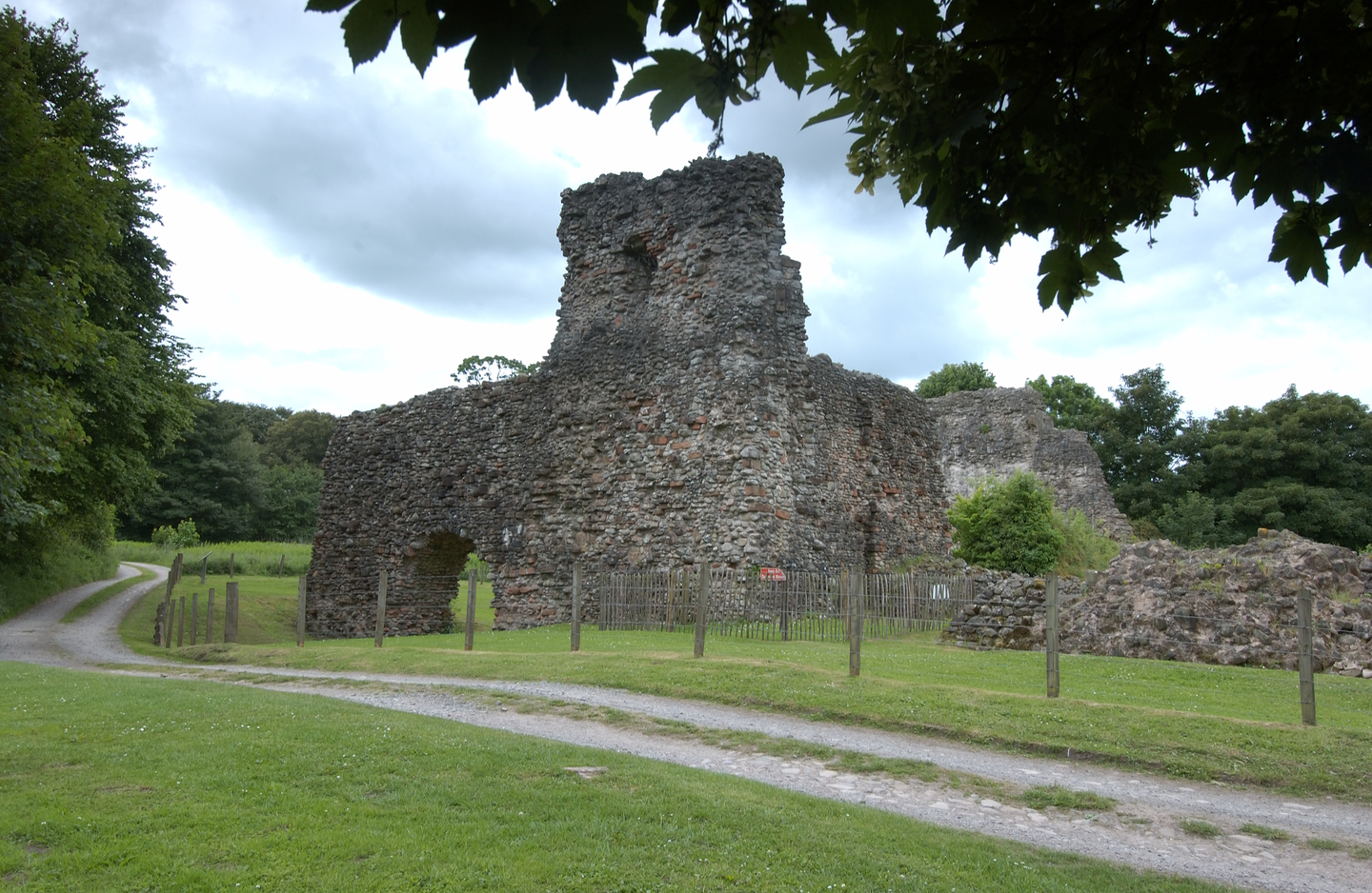 Remains of a stone castle. Only part of the castle is remaining, with parts deteriorated more than others. There is a small arch in part of it. You can see a road in front of the Castle remains, with a gate separating the road and site.  