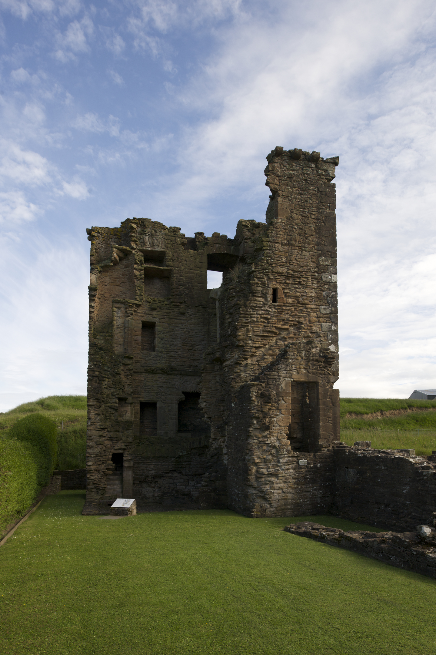 Ruined tower house at Crossraguel Abbey with exposed stonework and missing sections, standing beside a neatly cut grass area.