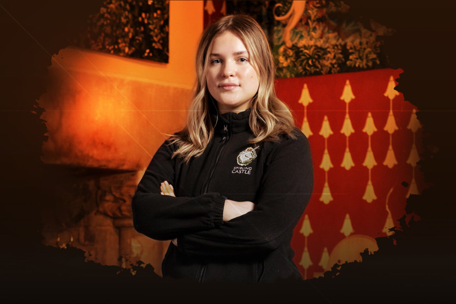 A person standing with their arms crossed with some tapestries on the wall behind them