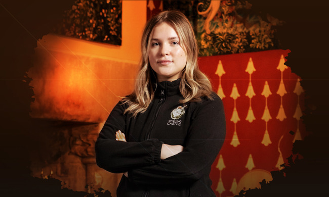 A person standing with their arms crossed with some tapestries on the wall behind them
