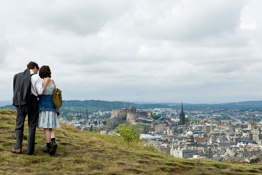 Two of the main characters from One Day standing on Arthur's Seat looking over Edinburgh, including a view of the castle