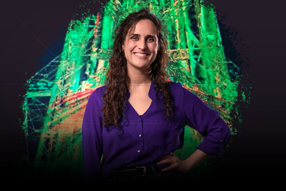 A woman with her left hand on her hip and smiling, and a 3D scan displayed on a wall behind her