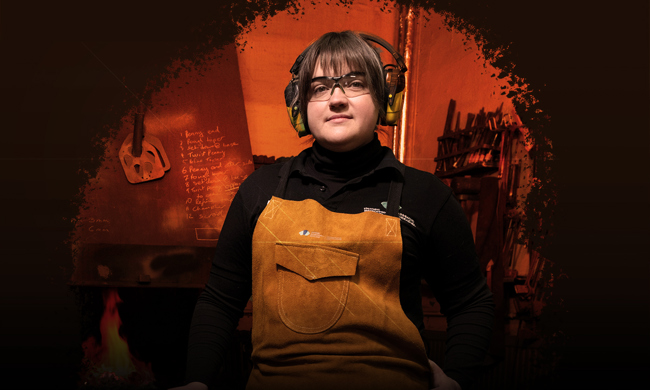 A woman wearing HES branded bib and brace overalls, protective glasses and ear defenders