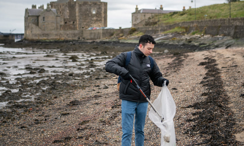 A person with a bin bag and grabbers collecting rubbish from a beach