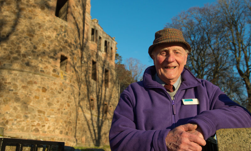 A man standing on a drawbridge wearing a hat and a purple HES volunteer fleece