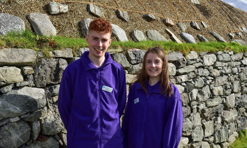 Volunteers, Alex John (left) & Lauren Matheson (right) standing outside the Blackhouse, Arnol