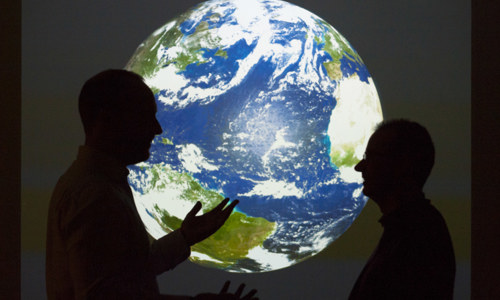 Two people talk against a projected backdrop showing Earth.