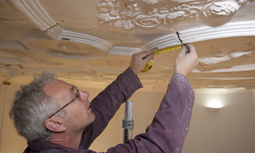 A contractor looking at some ceiling plasterwork inside a traditional building.