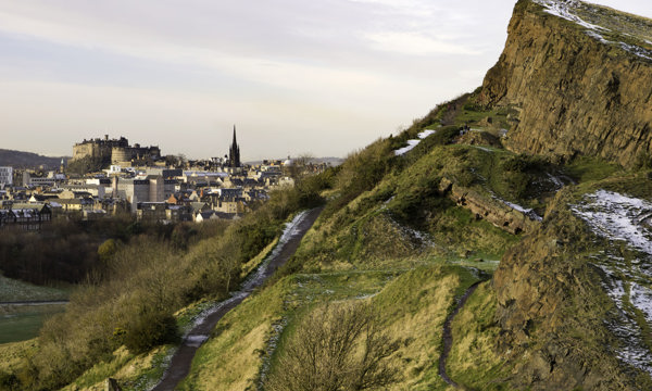 A view of a snowy Salisbury Crag, with Edinburgh Castle visible in the background.