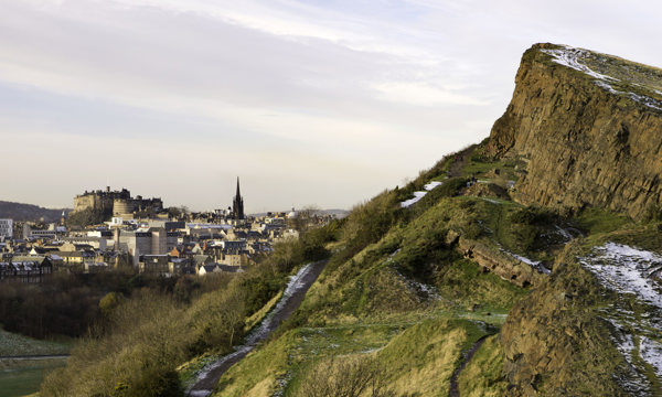 A view of a snowy Salisbury Crag, with Edinburgh Castle visible in the background.