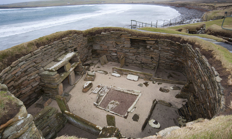 A look down into a now-roofless building with stone furniture at Skara Brae prehistoric village.