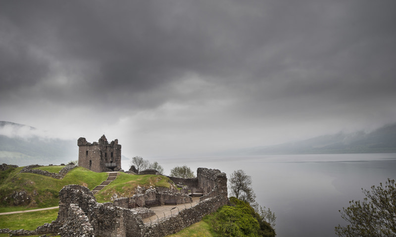 A moody view of Urquhart Castle and Loch Ness on a cloudy, foggy day.