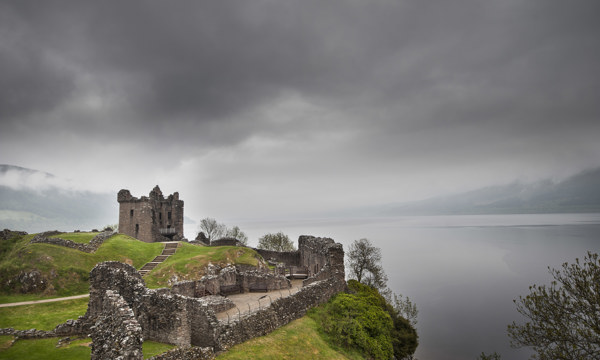 A moody view of Urquhart Castle and Loch Ness on a cloudy, foggy day.