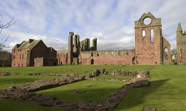 A general view of the ruins of Arbroath Abbey, with some stone foundations visible in the foreground.
