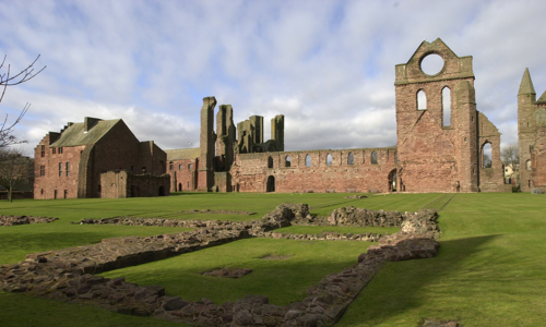 A general view of the ruins of Arbroath Abbey, with some stone foundations visible in the foreground.