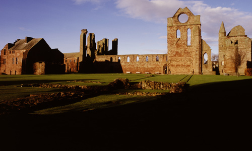 A general view of the ruins of Arbroath Abbey, with some stone foundations visible in the foreground.