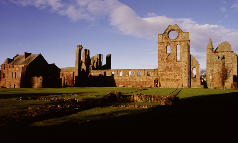 A general view of the ruins of Arbroath Abbey, with some stone foundations visible in the foreground.