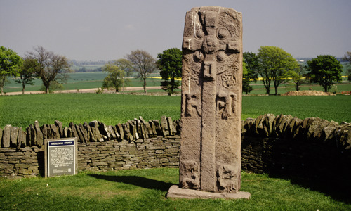 Aberlmeno Sculptured Stone with a low stone wall and a grassy plane in the background