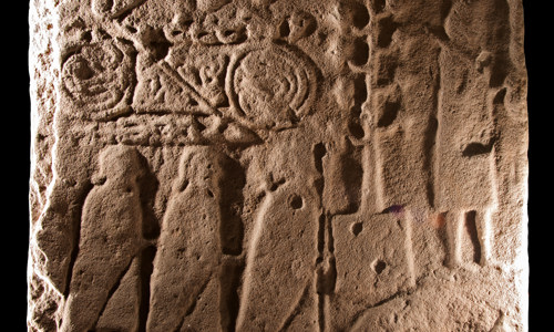 A detailed view of Eassie Sculptured Stone. The back of the stone is decorated with a number of things including a double-disc and z-rod, a Pictish beast, three men with cloaks carrying spears and several cows with scroll joints.