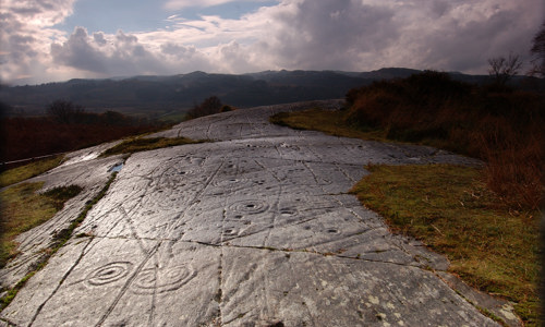 Smooth stone ground is covered in carved marks, including spirals and circles. 