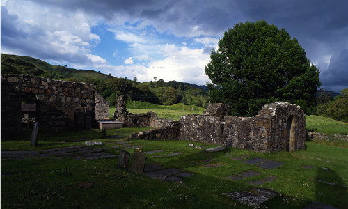 The ruins of Ardchattan Priory with a large oak tree in the background on a cloudy day