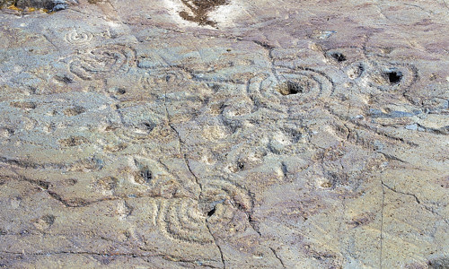 Holes surrounded by concentric circles are carved into the rockface.