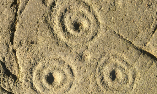 Holes surrounded by concentric circles are carved into the rockface