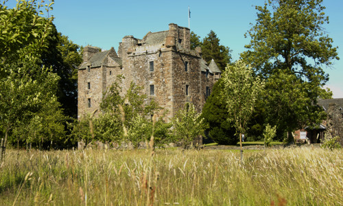 Well-preserved Elcho Castle with its several towers, surrounded by trees and fields.