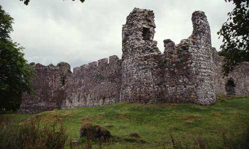 A ruined round tower hugged by two stone walls leading to other parts of the castle.