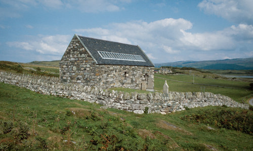 A stone cottage with a silver ladder-like part on the stone roof,  in a rural landscape.