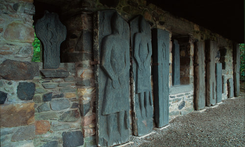 Several large sculptured stones portraying people in various poses are propped up against a roofed wall.