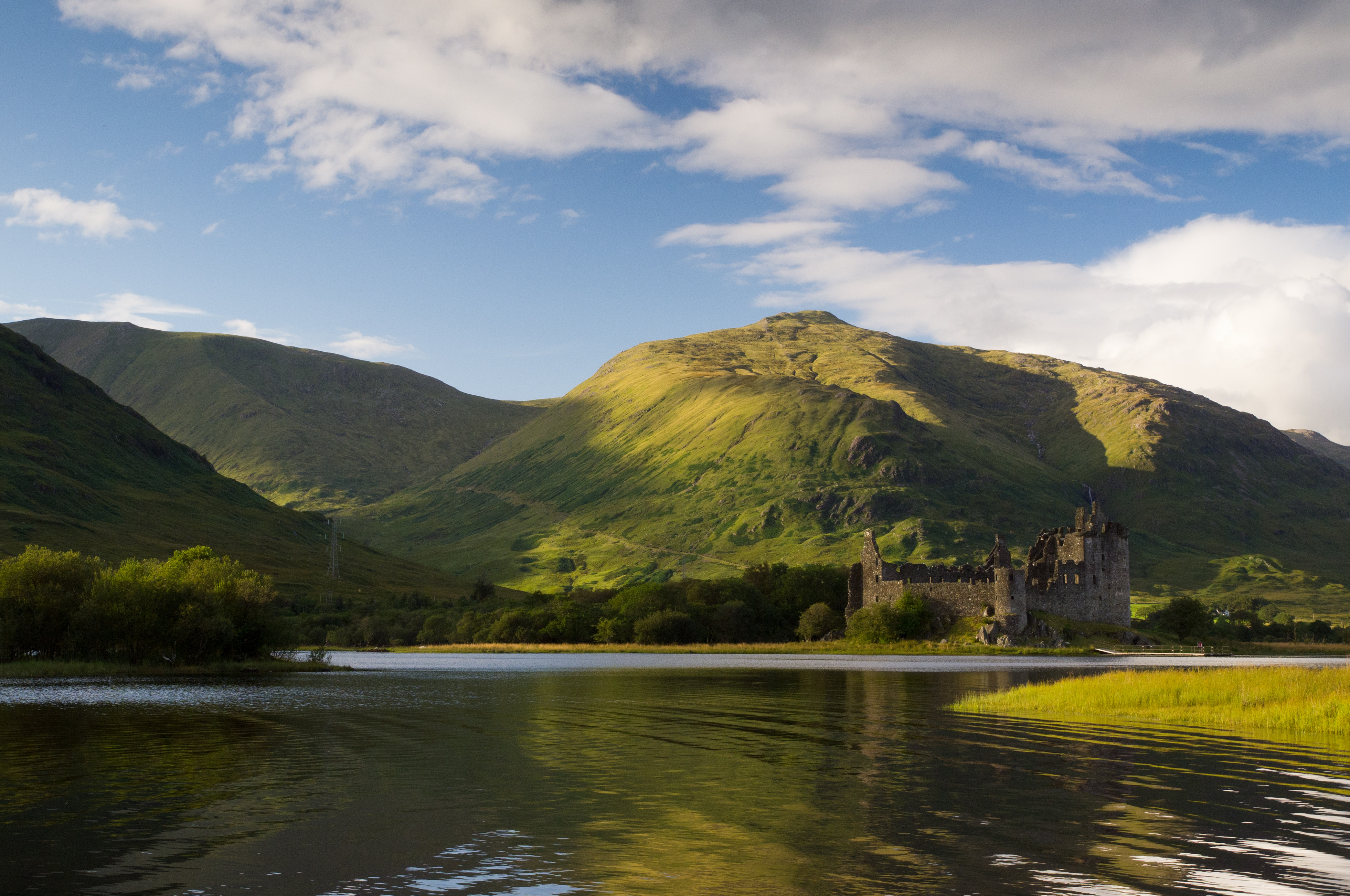 The very picturesque Kilchurn Castle viewed from Loch Awe, with sun-touched hills just behind it.