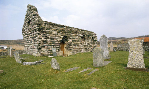 The ruins of a small stone chapel surrounded by grave slabs.